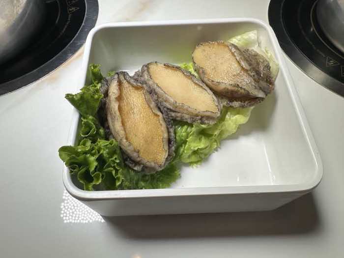 Giant abalone at Hot Lava Pot Three giant abalone served on lettuce in a white dish beside a hot pot burner
