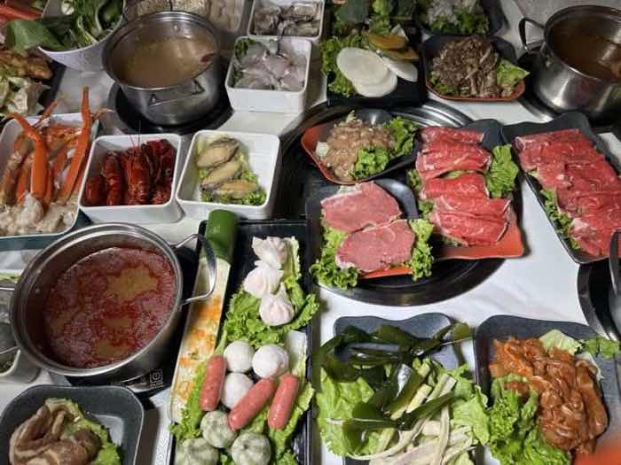 Platters of sliced beef and vegetables surrounding a pot of spicy red broth