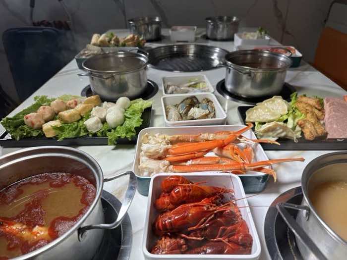 Snow crab legs and whole crawfish plated in front of simmering broth pots and fish balls