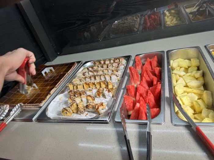 A chilled self-serve bar with trays of sliced watermelon, pineapple and pastries