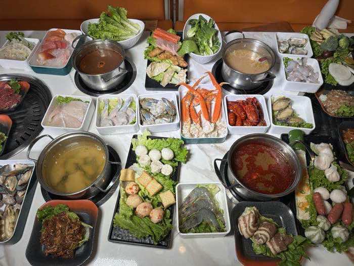 Two hot pots with different broths surrounded by fresh seafood, meat and vegetable dishes