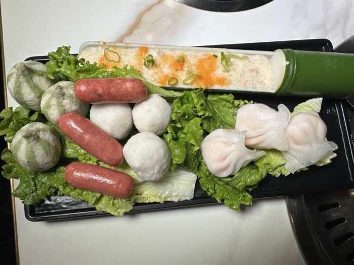 Hot pot sides and dumplings Shumai, fish balls, sausages and dumplings arranged on lettuce on a black serving tray