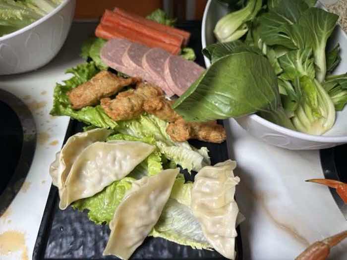 Dumplings, fried chicken pieces, sliced sausage and a bowl of bok choy on a black tray