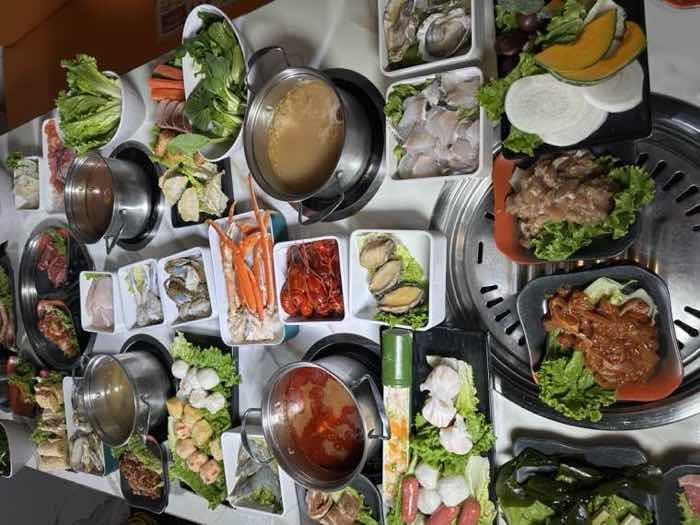 Overhead view of a long table filled with broth pots, seafood, marinated meats and vegetable dishes