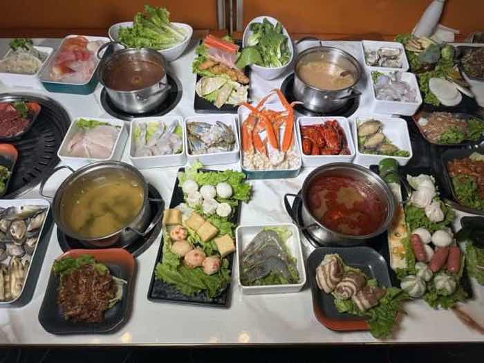 A full seafood feast A fully set table covered with crab legs, prawns, sliced fish, vegetables and three broth pots