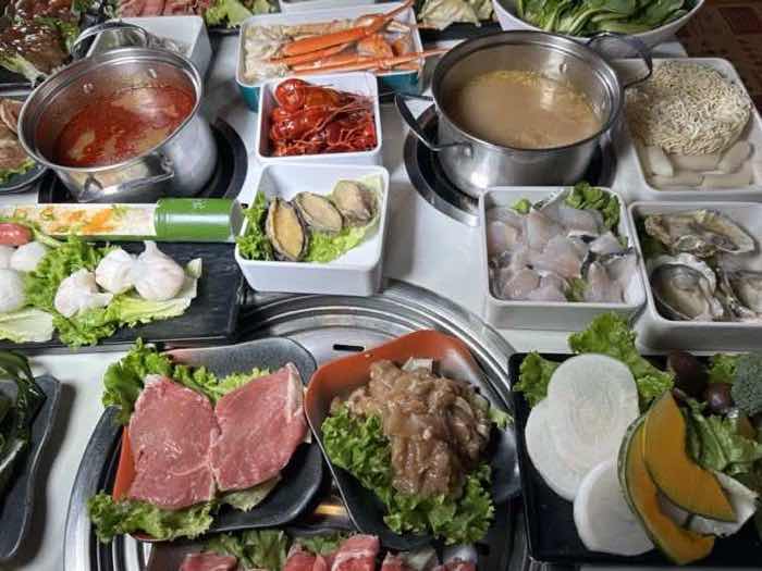 Kimchi, crab legs, crawfish, oysters and sliced fish set around two broth pots and a grill