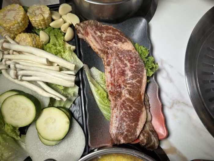 Marbled steak with corn and mushrooms A thick marbled steak on a black plate beside grilled corn, king oyster mushrooms, zucchini and garlic