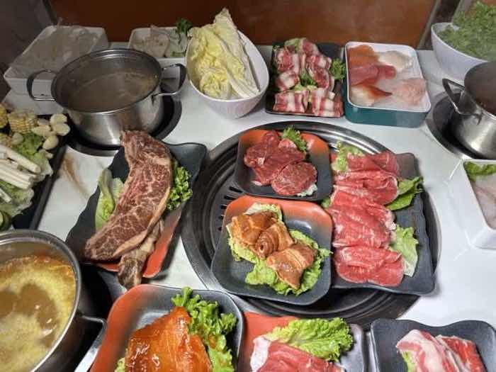 A bone-in short rib and several platters of sliced beef arranged around a built-in grill
