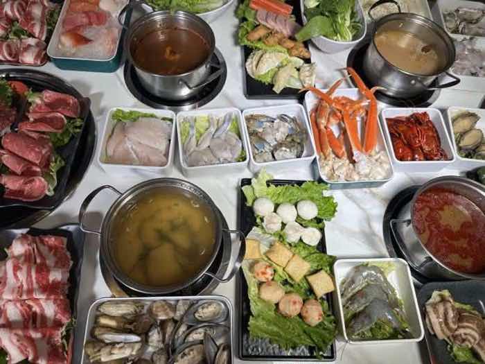 Overhead view of crab legs, prawns, sliced fish and mussels around pots of golden and red broth
