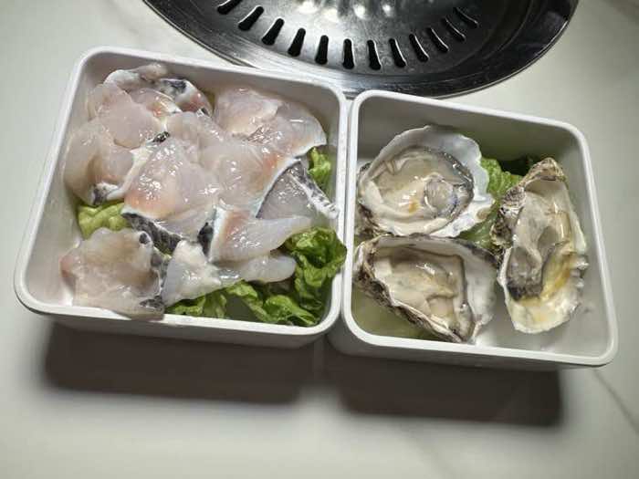 Sliced white fish fillets and oysters on the half shell in two white dishes beside the grill