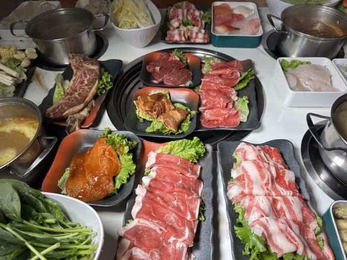 Steak, pork belly and sliced beef platters set around a grill with a pot of golden broth