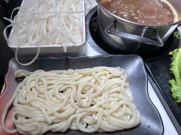 Udon and rice noodles A plate of thick udon noodles and a tray of thin rice noodles beside a simmering broth pot